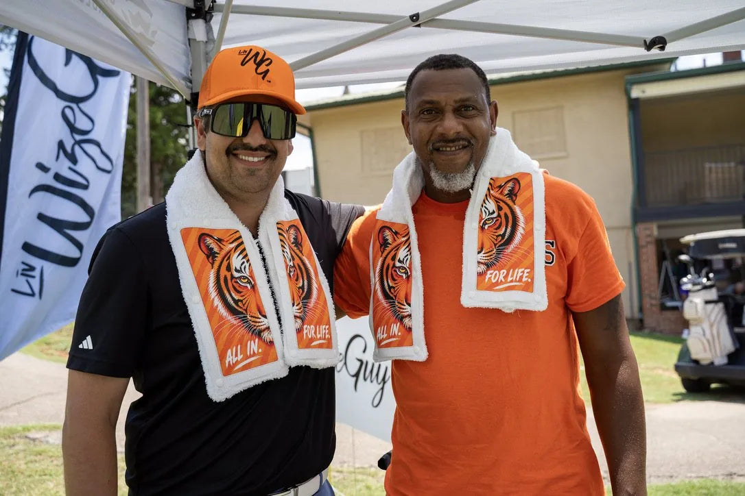 Two golfers wearing Tiger towels in front of the LivWizeGuy banner