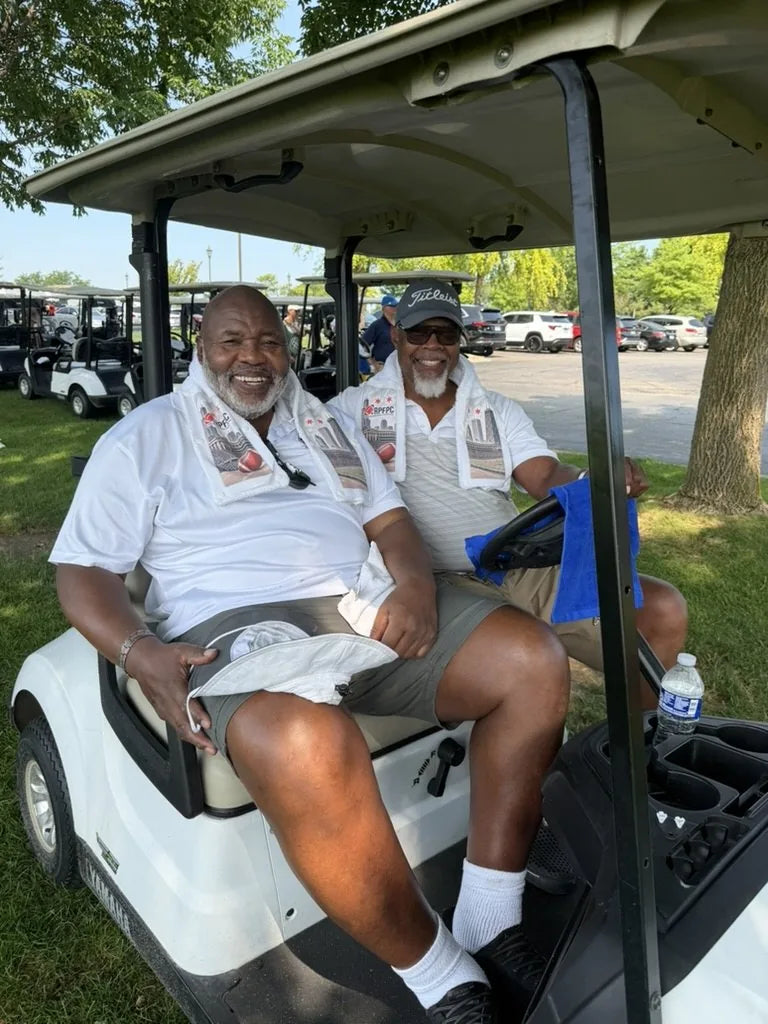 Two players in a golf cart wearing LivWizeGuy towels