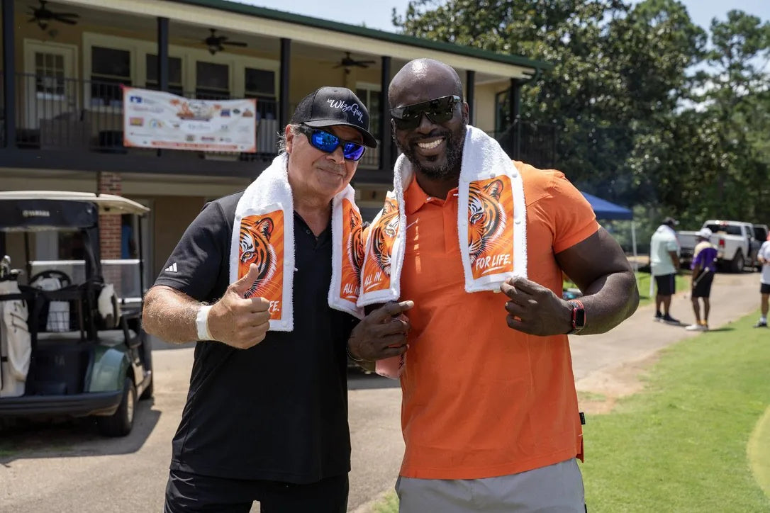 Two golfers giving a thumbs up in Tiger towels by the clubhouse